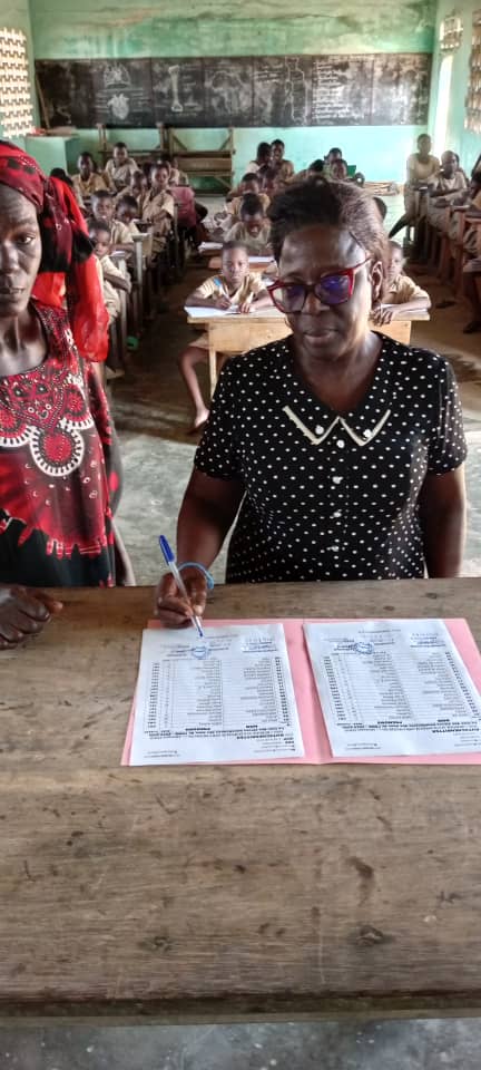 Übergabe an der Grundschule Kutschenritter in Aného, Togo: eine Verantwortliche unterschreibt die Dokumente im Klassenzimmer, im Hintergrund lernen die Schülerinnen und Schüler.
