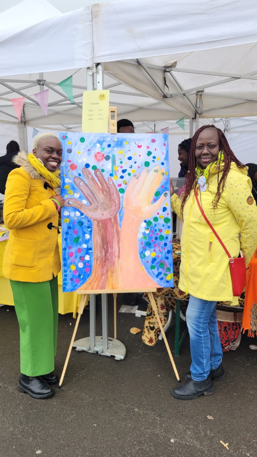 Zwei Frauen der Kette der Solidarität e.V. präsentieren ein gemaltes Hände-Kunstwerk an einem Stand