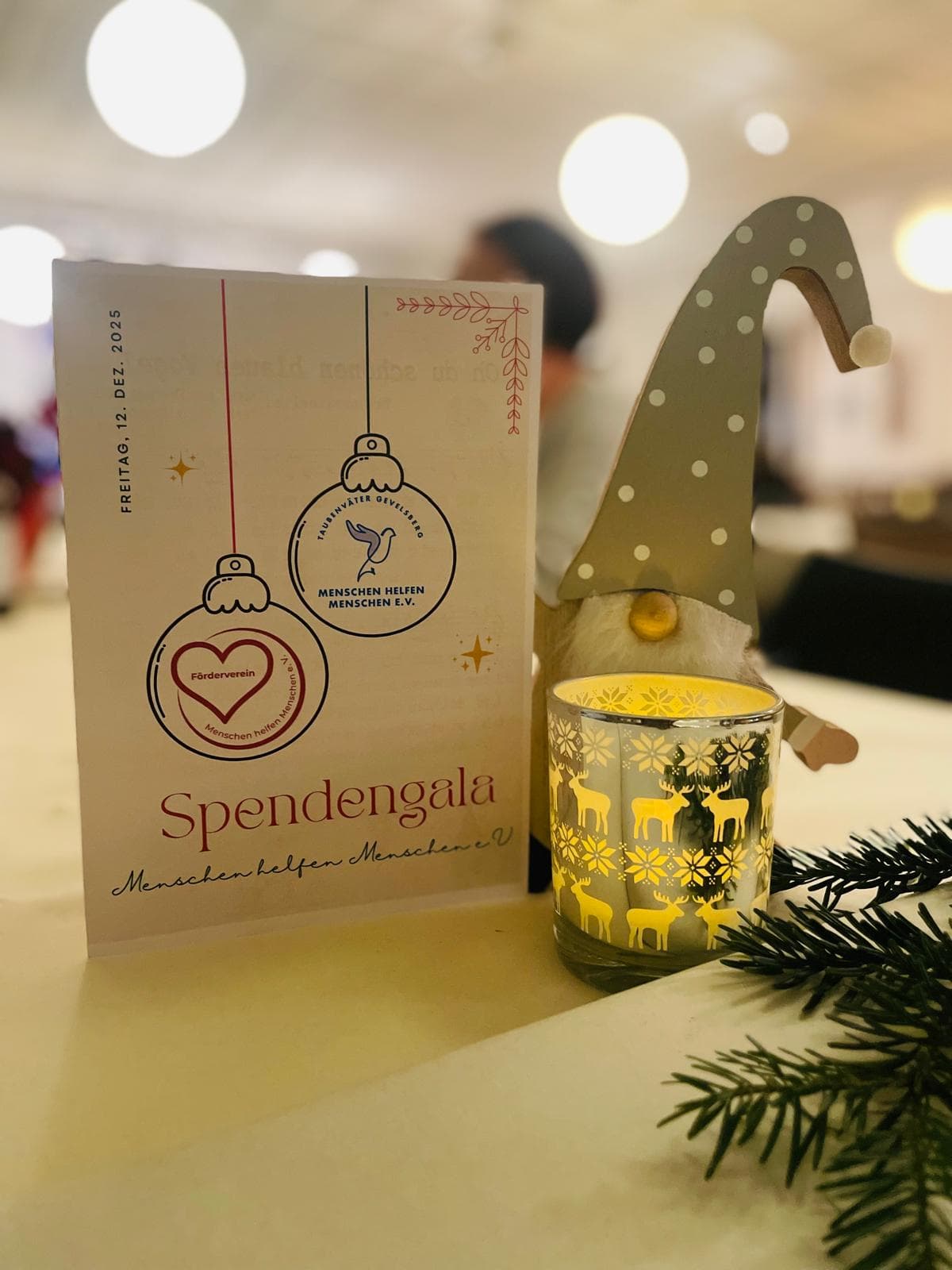 Programmkarte der Spendengala „Menschen helfen Menschen e.V.“, Freitag 12. Dezember 2025, mit weihnachtlicher Tischdekoration